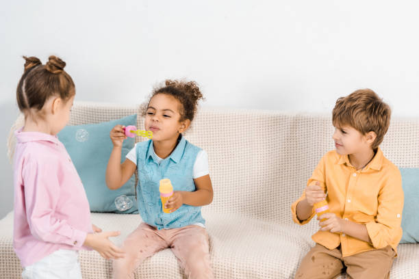 istock adorable multiethnic kids sitting on sofa and blowing soap bubbles 1078051350