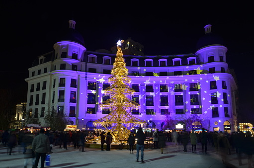 Bucharest, Romania - December 1, 2018: People enjoy their free evening time in Christmas market decorated with beautiful artificial Christmas tree, set up in University Square.