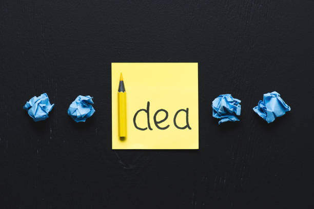 istock 'idea' word written on sticky note and blue crumpled paper balls on black background, ideas concept 1078060406