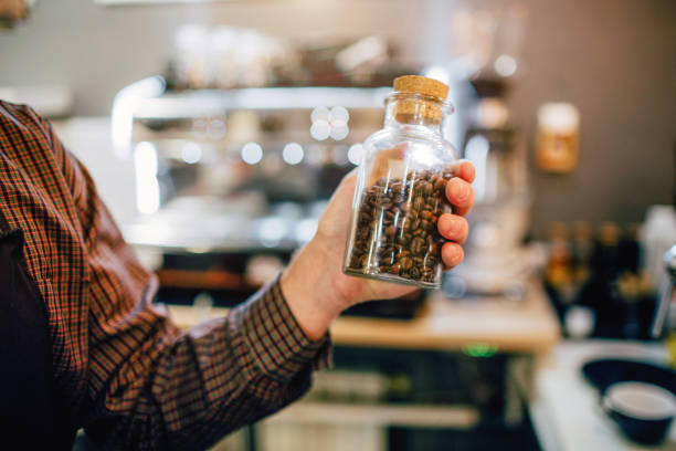 istock Man hold glass on coffee beans in hand. He stands inside in kitchen. Cut view. 1078070598