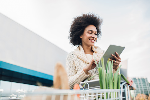 Smiling girl pushing shopping cart and looking at digital tablet