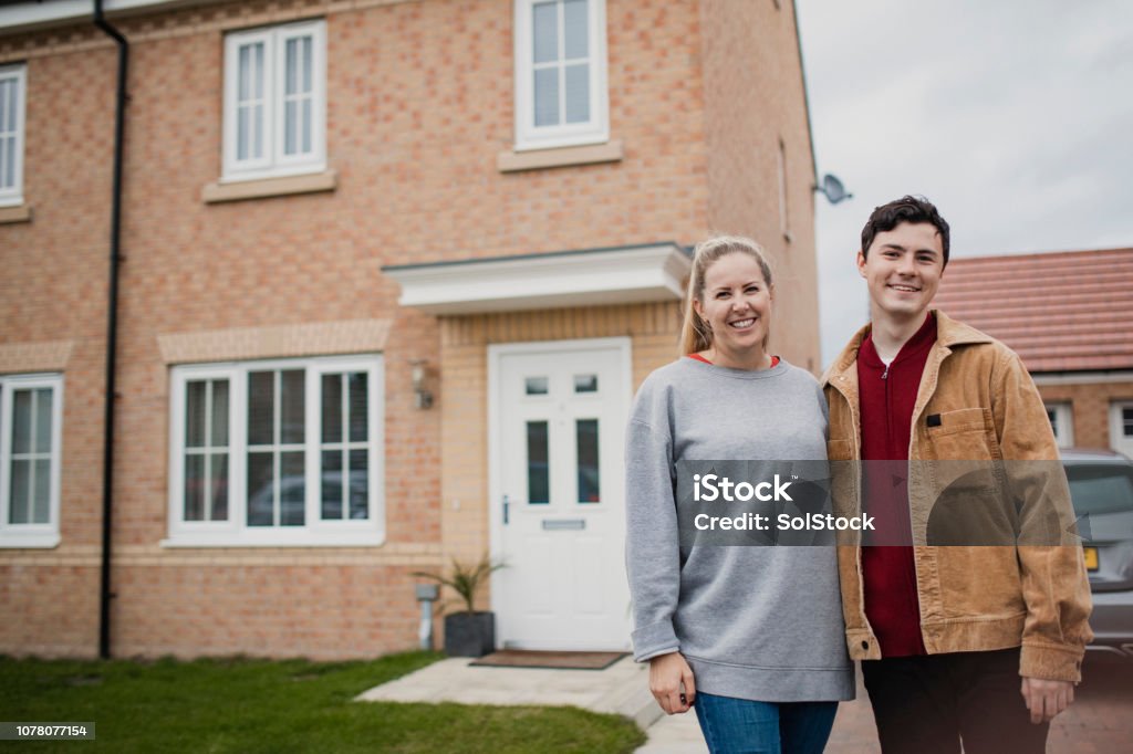 Couple Standing Outside New Home A wide-view shot of a young couple standing outside their new home, they have wide smiles on their faces. House Stock Photo