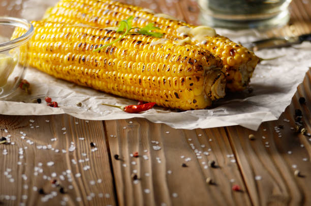 istock Kitchen table with grilled sweet corn cob under melting butter and greens on baking paper 1078088228