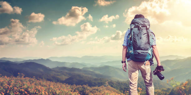 istock A young guy with a backpack traveler standing on a cliff holding camera and watching White misty mountains. Travel photo lifestyle 1078093614