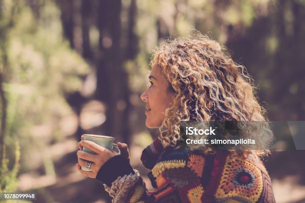 Beautiful Woman In Autumn Forest Enjoying The Feeling With The Nature With A Warm Sweater Lady Sits With Trees In Background In A Forest And Holds A Cup With A Hot Drink In Her Hands Girl Travel And Wanderlust Millennial Concept Stock Photo - Download Image Now