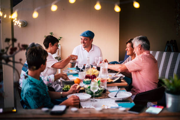 dinner time in friendship with different ages people all together having fun and enjoying the night with smiles and happiness. mobile phones defocused in for technology modern concept - food vegan food gourmet vegetarian food imagens e fotografias de stock