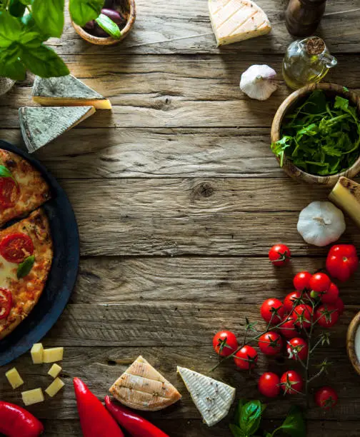 Pizza on wood with ingredients. Pizza with cheese, tomatoes and basil. Rustic italian pizza