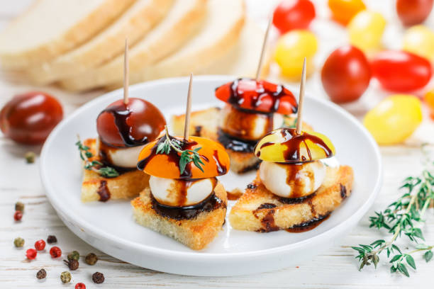 bread toast with tomato cherry, mozzarella cheese, thyme and balsamic glaze on white wooden background. canape. bruschetta. gourmet snack. selective focus - baguette vinegar balsamic vinegar glazed imagens e fotografias de stock