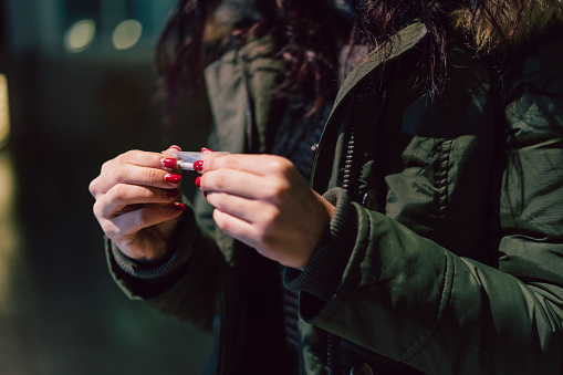 Young adult woman rolling a cigarette outdoor in the city at night