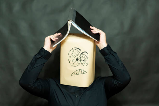 concepto de emoción. un hombre está albergando desde arriba de la precipitación. sostiene un libro abierto sobre su cabeza. la expresión se centra y tensa. - human hand sheltering men making fotografías e imágenes de stock