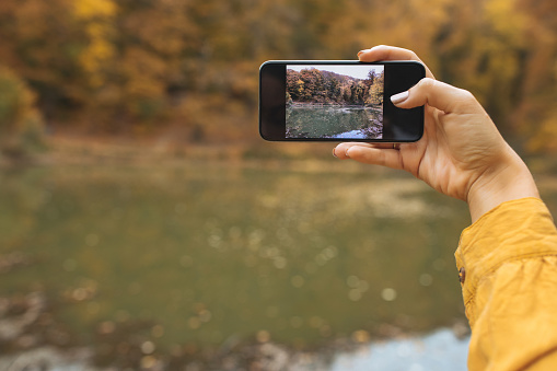 Close up of female hand holding phone and taking a picture of beautiful landscape