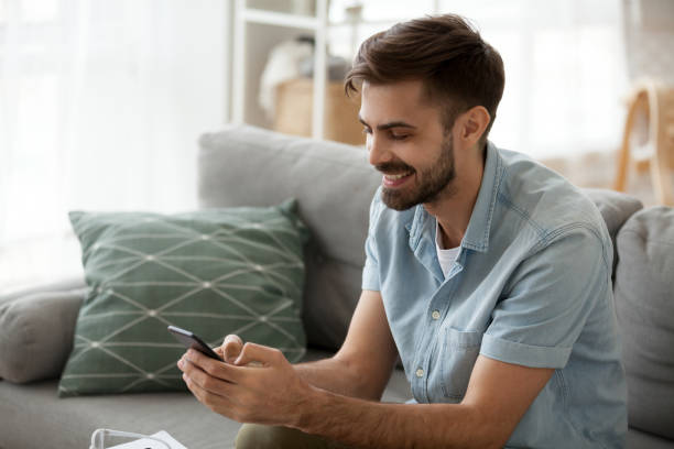 istock Excited male sit on couch using smartphone texting to friends 1078149240
