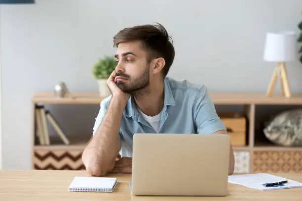 Photo of Tired man distracted from computer work lacking motivation