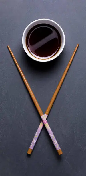 A cup of soy sauce with crossed chopsticks over gray slate
