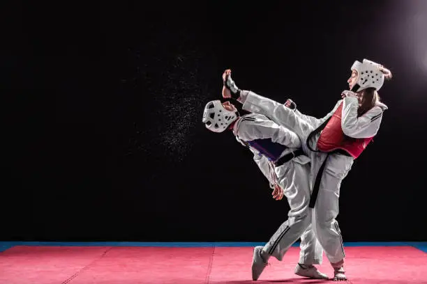 Young man and woman in taekwondo combat. Girl beating against man while punching him with leg in his head. Fight of two black belts