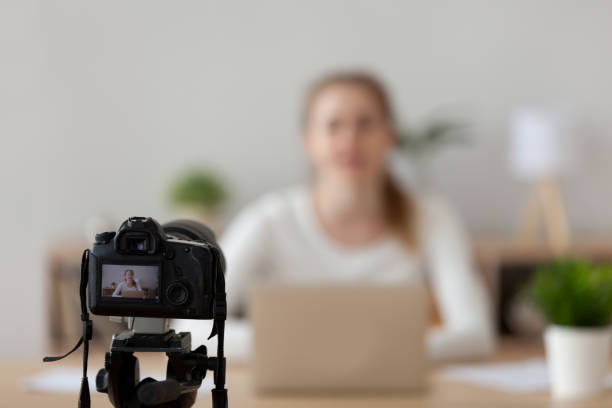 Professional camera shooting female filming tutorial at home Professional camera shooting online video course of female coach or speaker talking, woman film tutorial sitting on desk with laptop, girl blogger record live blog, speaking on camcorder device audio electronics stock pictures, royalty-free photos & images