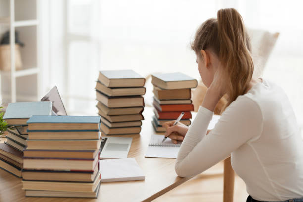 istock Focused girl writing in notebook surrounded by books at table 1078156296