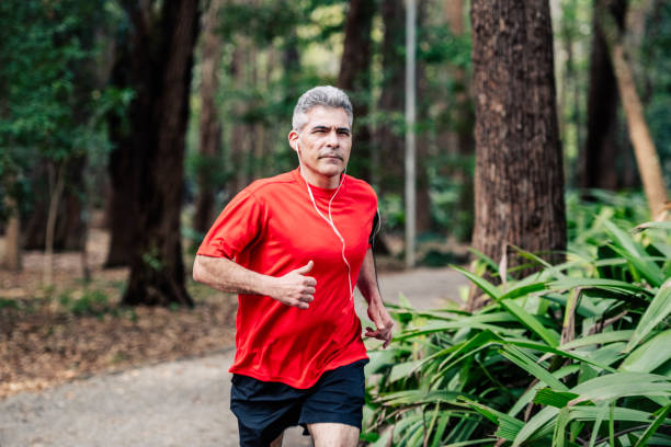 Mature man jogging in woods with earphones Healthy man with grey hair running in park, training, wearing earphones, escapism, active seniors one mature man only audio stock pictures, royalty-free photos & images
