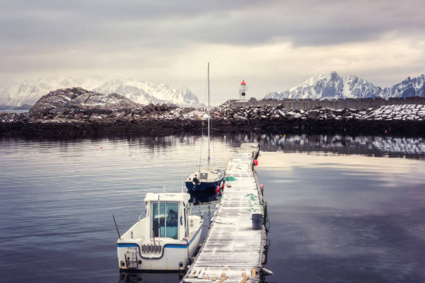 cais de madeira com barcos de pesca, farol e nevadas montanhas, paisagem de inverno, kabelvag, ilhas lofoten, noruega - lofoten lighthouse winter waterbreak - fotografias e filmes do acervo