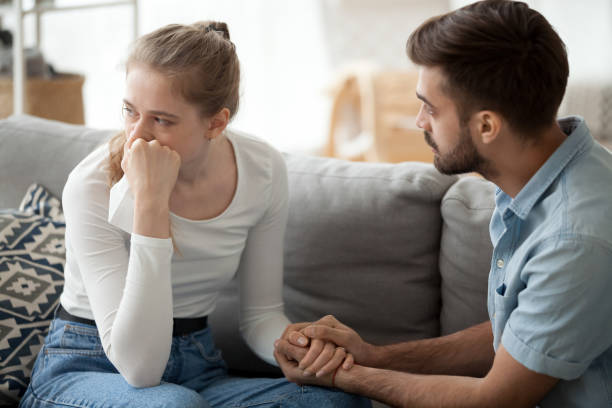 Caring husband hold wife hand making peace after fight Loving young husband hold crying wife hand showing empathy and support, millennial couple sit on couch at home reconcile after fight, caring man making peace with beloved woman. Relationships concept wife stock pictures, royalty-free photos & images