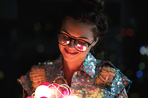 Christmas, New year or another celebration concept. Happy woman wearing glowing jacket with sequins is holding light balls in her hands.