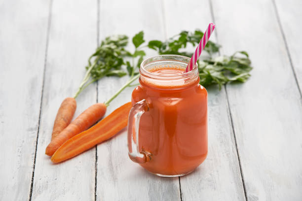 juice in a glass container surrounded by fresh vegetables and fruits on white boards