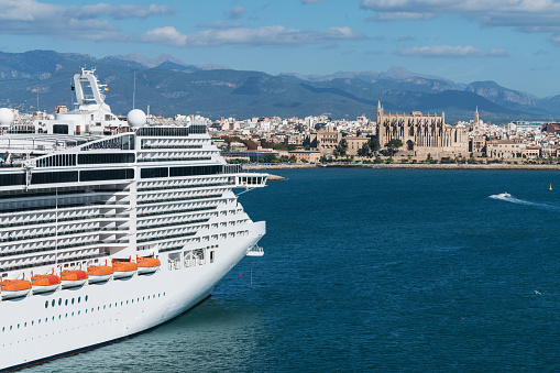 Palma, Balearic Islands, Spain – November 7, 2018: A large cruise ship moored at the port of Palma de Mallorca at daytime. In the distance the Gothic Roman Catholic cathedral of Santa Maria of Palma (La Seu) can be seen in the center of the city.