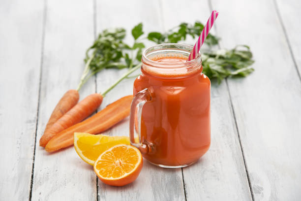 Healthy vegetable and fruit juice juice in a glass container surrounded by fresh vegetables and fruits on white boards carrot juice stock pictures, royalty-free photos & images