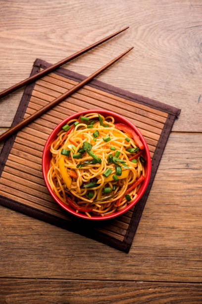 Schezwan Noodles or vegetable Hakka Noodles or chow mein is a popular Indo-Chinese recipes, served in a bowl or plate with wooden chopsticks. selective focus stock photo