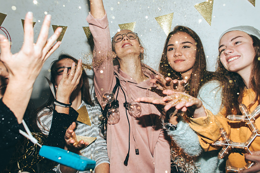 Photo of a smiling teenage girls having fun while celebrating New Year's Eve and tossing confetti in the air