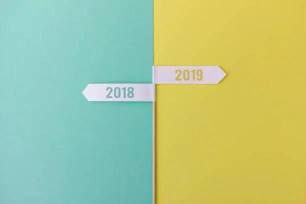 Minimalist composition of wood stick with flags showing towards the years 2018 and 2019 on colorful background