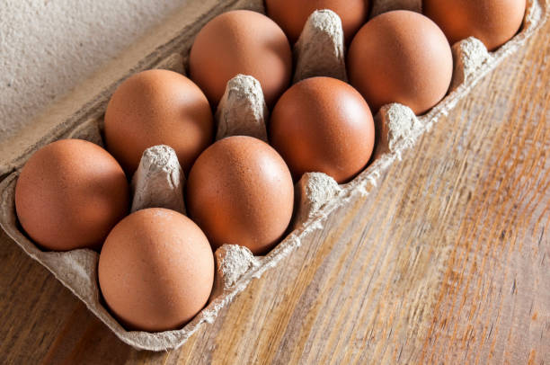 istock Large brown chiken eggs in carton package on brown wooden table. 1078214492