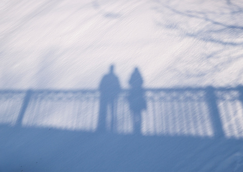 Shadow silhouette of couple man and woman standing on a bridge on snow background on sunny winter day