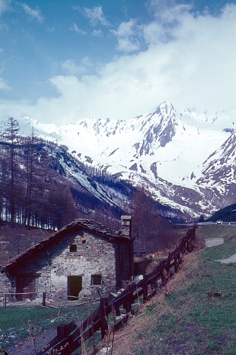 Valais canton, Switzerland, 1968. Cloud-covered St. Bernhard. In the foreground an old uninhabited farmhouse.