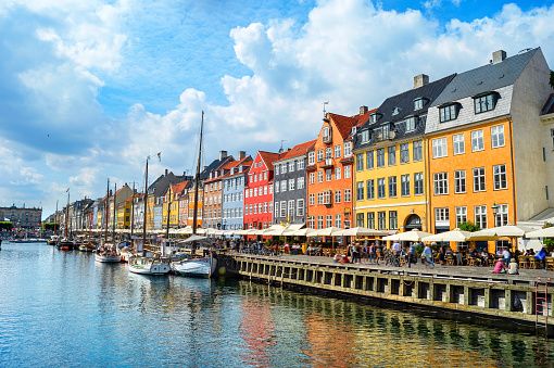 People walking at sunny Nyhavn embankment with moored boats, Copenhagen, Denmark