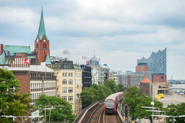Metro train passing by Hamburg embankment with clock tower and Elbphilharmonie building at background, Germany