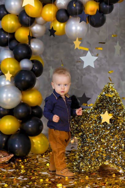 istock Handsome boy posing on party decorations with huge big golden star. Grey background. silver stars and different balloons. 1078226320