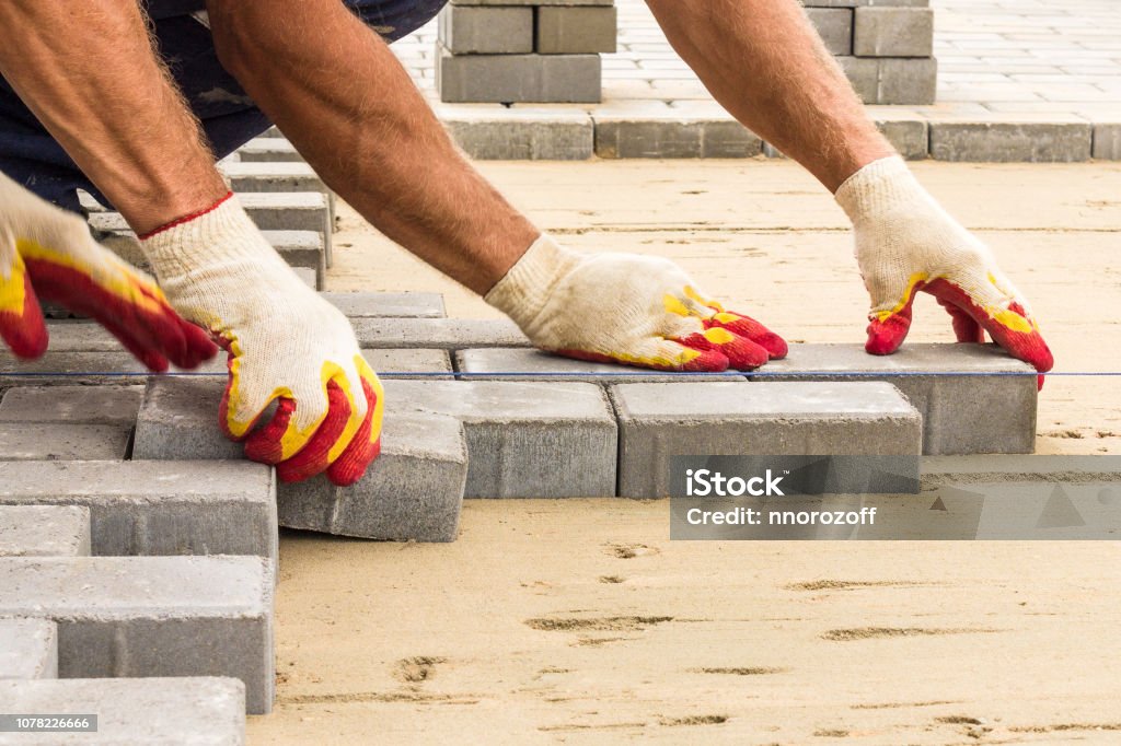 workers lay paving tiles, construction of brick pavement, close up architecture background workers lay paving tiles, construction of brick pavement, men's hands in gloves, close up architecture background Paving Stone Stock Photo