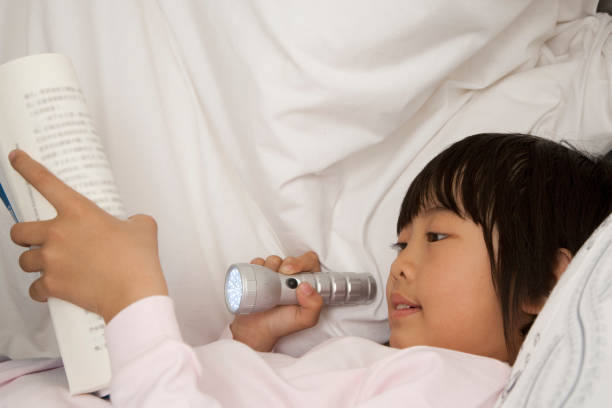 istock Chinese boy reading book by flashlight in bed 1078229420