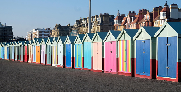 A line of twenty five multi coloured beach huts on Brighton promenade with a diminishing perspective, the sun is shining with a blue sky.