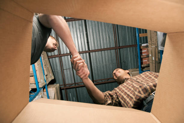 secouant l’homme remet une boîte en carton dans l’entrepôt - business relationship cooperation business handshake photos et images de collection