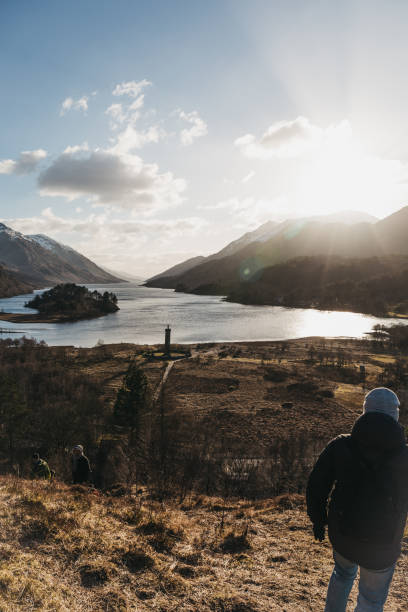 People hiking in Glenfinnan, Scotland, Glenfinnan Monument on the background. Glenfinnan, Scotland - March 17, 2018: People hiking in Glenfinnan, Glenfinnan Monument on the background. The monument was erected is 1745 and is cared for by the National Trust for Scotland. glenfinnan monument stock pictures, royalty-free photos & images