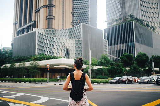 Young brunette woman traveling alone in Singapore. She is admiring the amazing combination of vegetation and architecture in the beautiful Southeastern Asian city.