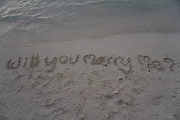 wording "Will you marry me?" which hand writing on sand with sea background