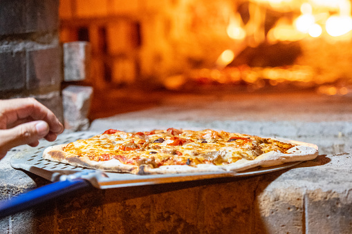Cook cooking Pizza in a wood fire Brick oven at a pizzeria