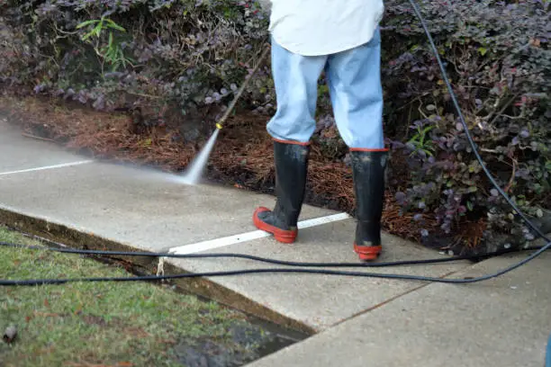 Photo of Worker pressure washing conrete sidewalk to clean it