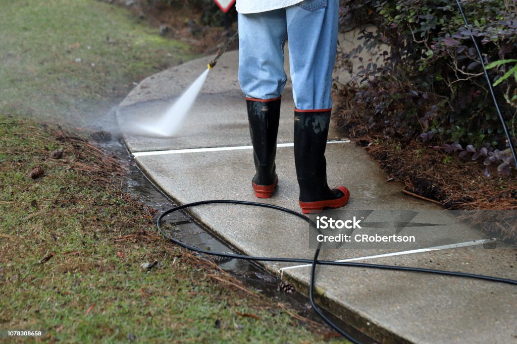 Worker pressure washing conrete sidewalk to clean it Worker pressure washing sidewalk of a home, to clean it and improve. High Pressure Cleaning Stock Photo