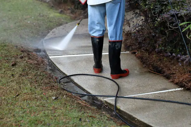 Photo of Worker pressure washing conrete sidewalk to clean it