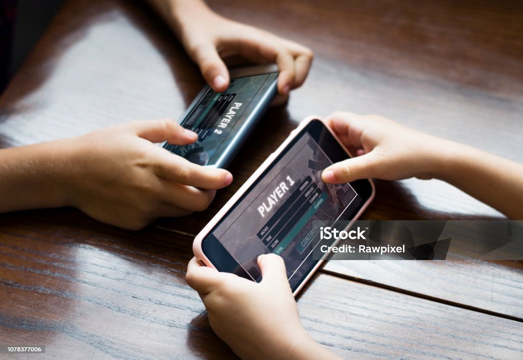 Garoto jogando um jogo para celular contra sua irmã - Foto de stock de Jogo de lazer royalty-free