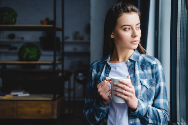 istock pensive young woman holding cup and looking at window 1078413866